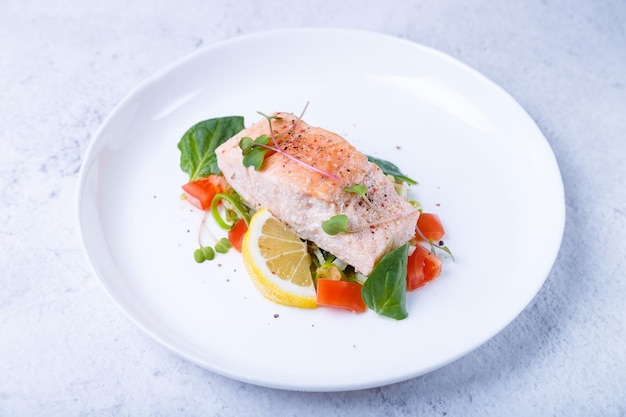 Trout (salmon) with vegetables, lemon and microgreens, cooked by the confit method. Traditional French dish. White background. Close-up.