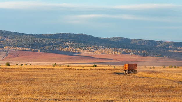 A truck drives along a country road in a field with a mountain in the background