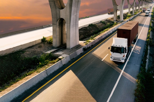 Truck on highway road with red container, transport on the asphalt expressway with sunrise sky