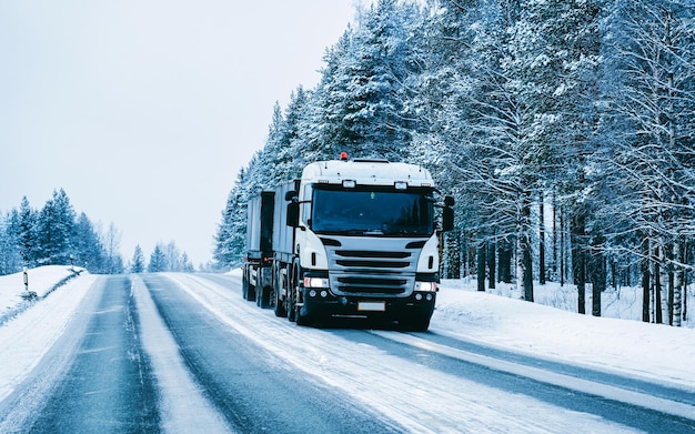 Truck in snow winter road of Finland. Trucker in highway. Lorry doing logistics work. Semi trailer with driver. Big cargo car drive. Freight delivery. Transport export industry. Container with goods