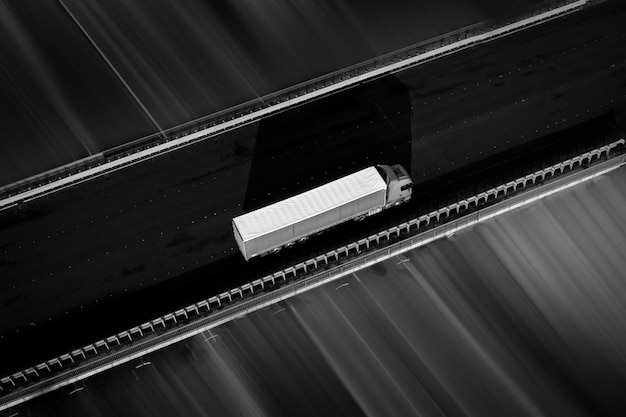 Truck with white trailer on a dark asphalt road  black and white photo