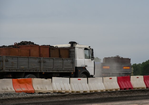 Trucks carrying cargo along a road under construction.