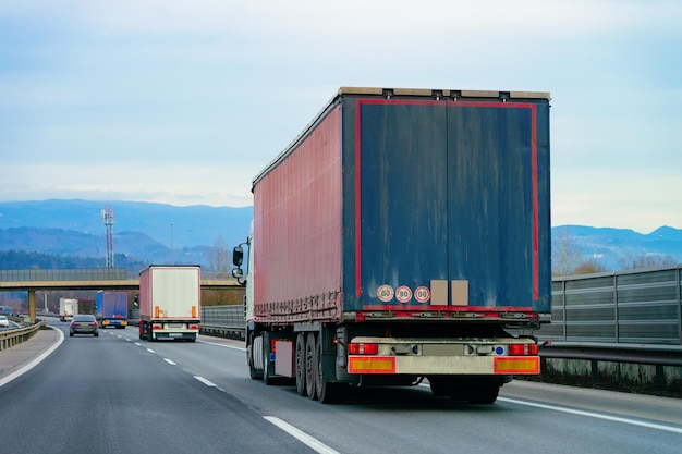 Trucks in road. Trucker in highway. Lorry doing logistics work. Semi trailer with driver. Big cargo car. Freight delivery. Transport export industry. Container with loaded goods on background.