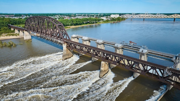 Truss arch bridge over large dam blue river water and white water rapids aerial of distant shore