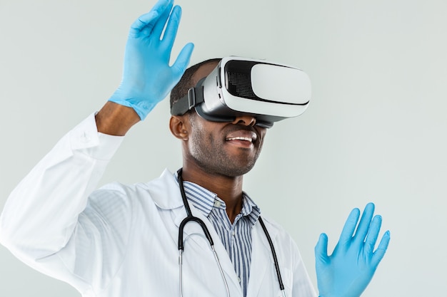 Try in action. Cheerful smiling doctor testing VR glasses while standing against white background