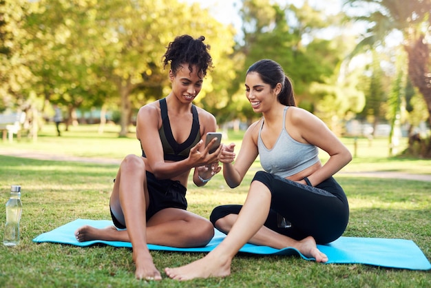 Trying to select the best filter Full length shot of two attractive young women sitting next to each other while using a cellphone in the park