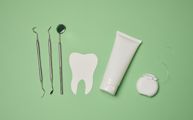 Tube with toothpaste dental floss and medical mirror on a green background oral hygiene