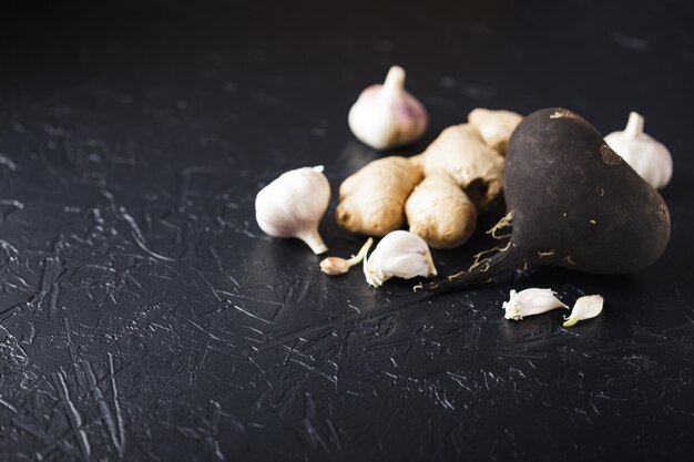 Tuber black radish and garlic on a black concrete surface