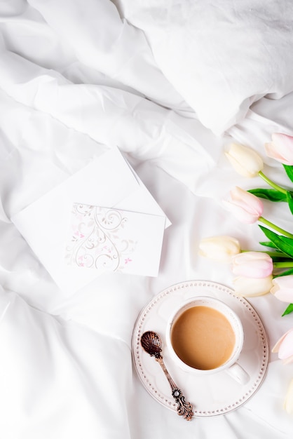 Tulips flower with cup of coffee and post card flat lay morning in bed 