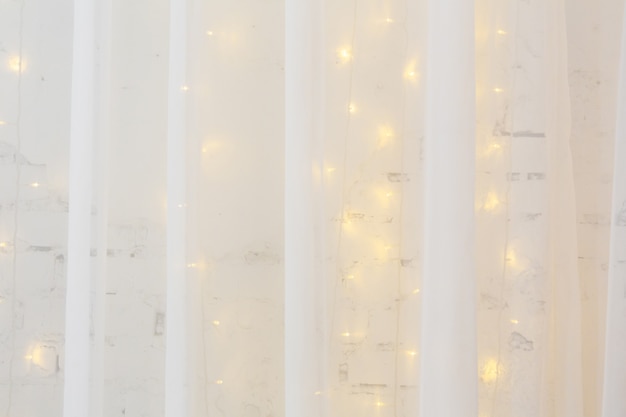 tulle curtain on background of white brick wall decorated with burning garland