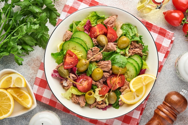 Tuna salad with fresh vegetables, olives, capers and lemon served in bowl on light grey background. Top view with copy space.