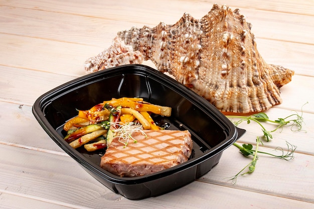 Tuna steak with grilled vegetables in containers on a white wooden background Takeaway Diet and healthy food