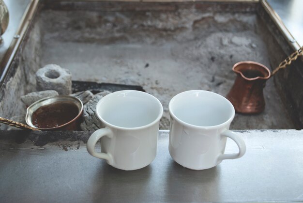 Turkish charcoal coffee. Coffee is being made over coals in a Turkish coffee cezve. Two cups stand on the surface near the coals.