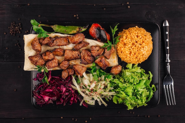 Turkish cuisine traditional shish kebab with bulgur and vegetables on a black plate