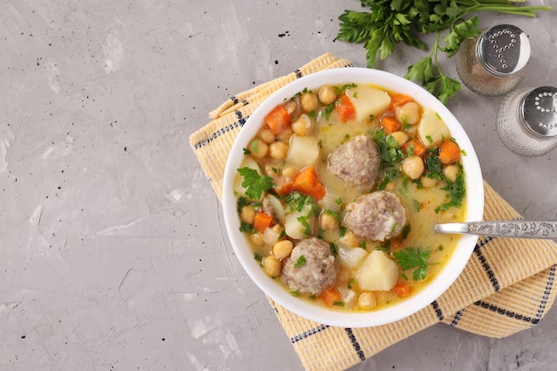 Turkish soup with chickpeas, meatballs and vegetables in a white bowl on a gray background