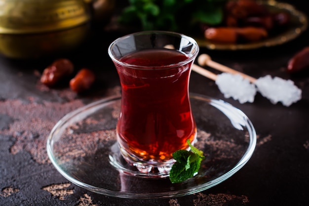 Turkish tea in traditional glass cup with caramelized sugar and mint on dark