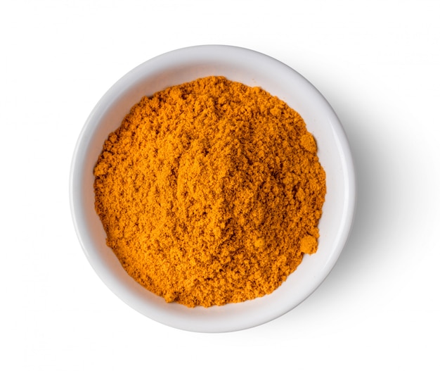 Turmeric powder in ceramic bowl on white wall. 