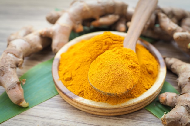 Turmeric powder and fresh turemric with green leaf in wood bowls on wooden table Herbal