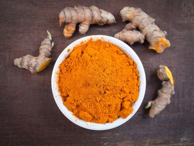 Turmeric powder and fresh turmeric in white bowls on old wooden table herbal