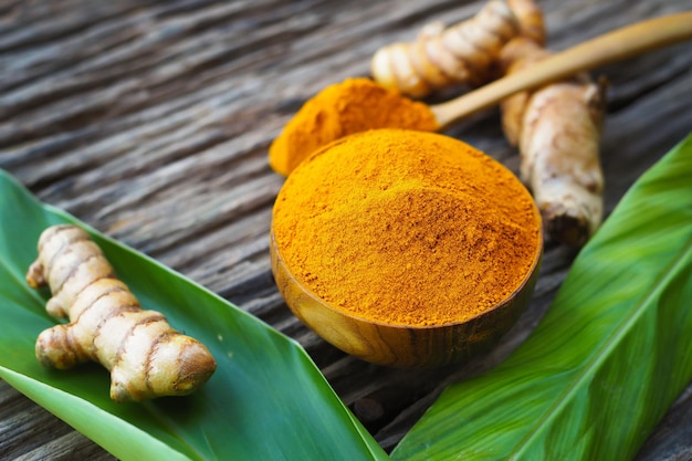 Turmeric powder and fresh turmeric in wooden bowls with green leaf on old wooden table. Herbs are native to Southeast Asia.