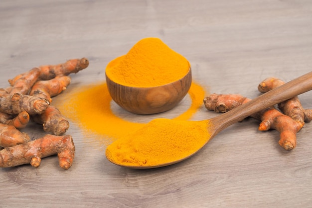 Turmeric powder and fresh turmeric in wooden spoon on old wooden table Herbs are native to Southeast Asia