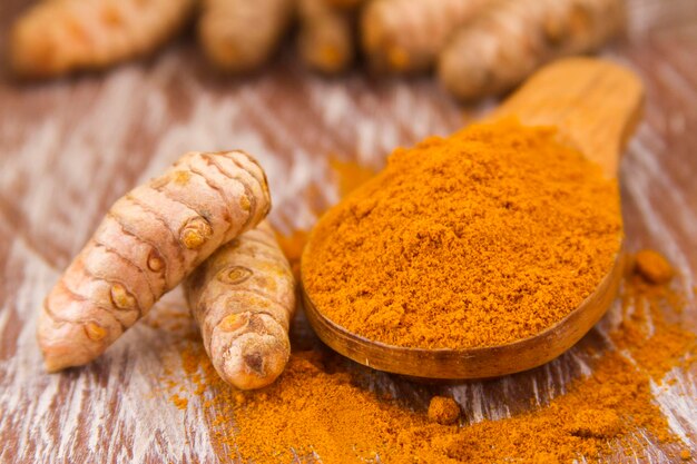 Turmeric powder and roots on wooden background