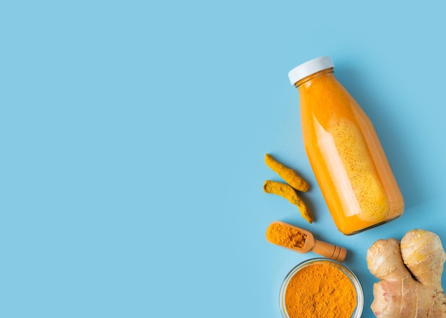 Turmeric smoothie in glass bottle with ingredients turmeric powder on blue background