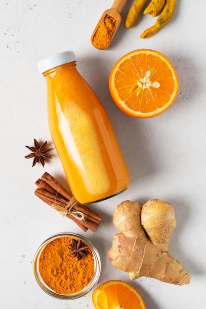 Turmeric smoothie in glass bottle with ingredients turmeric powder ginger and spice on white or light grey background