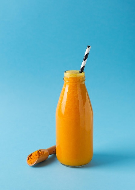 Turmeric smoothie in glass bottle with turmeric powder on blue background