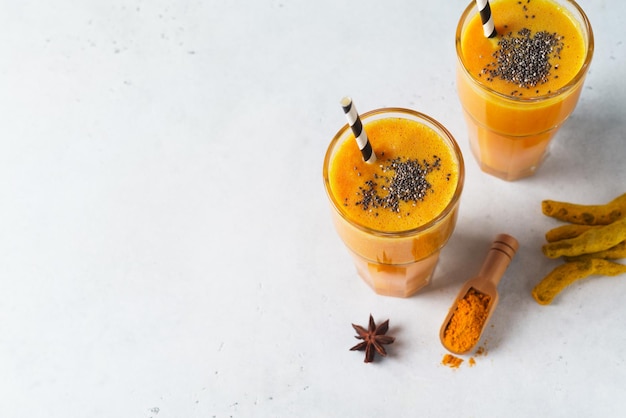 Turmeric smoothie in glass with ingredients powder ginger and spice on white or light grey background