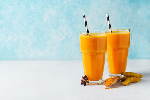 Turmeric smoothie in glass with ingredients turmeric powder ginger and spice on blue