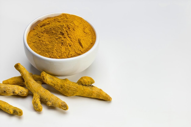 Turmeric tubers and ground turmeric in a white bowl Closeup studio shot