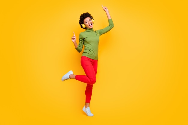 Turned full length body size portrait of cheerful positive cute pretty woman dancing at disco club with forefingers up in red pants white footwear.