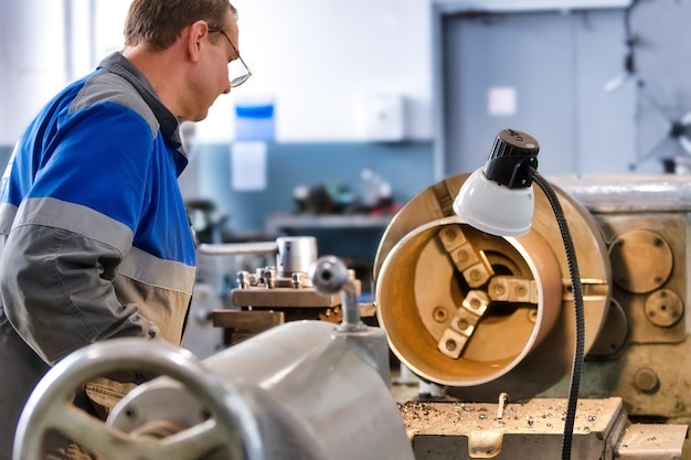 Turner in overalls works behind lathe in production hall Processing of metal products background