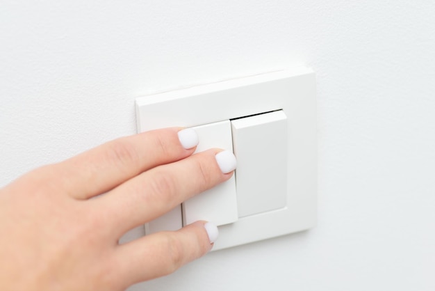 Turning on and off the light in the room with white walls Close up picture of female hand on light switch