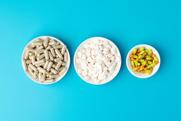 Turquoise background of large group of assorted capsules pills and tablets in white bowls in a row