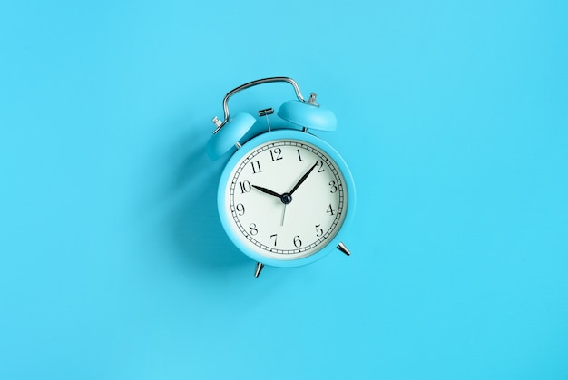 Turquoise blue vintage alarm clock on blue background. Top view, flat lay, copy space