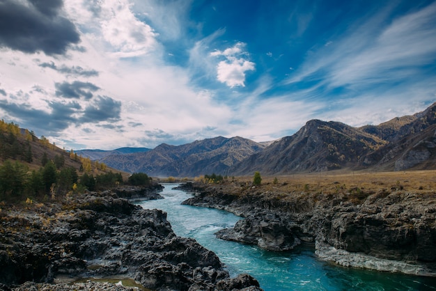 Turquoise Katun river in gorge is surrounded by high mountains under majestic autumn sky. A stormy mountain stream runs among rocks - landscape of the Altai mountains, beautiful places of the planet.