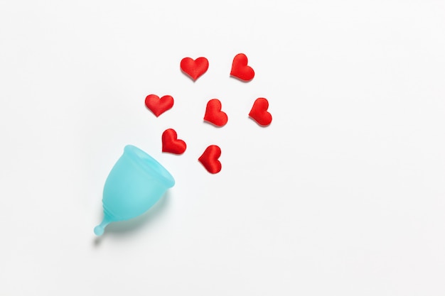 Turquoise menstrual cup on white background with red hearts