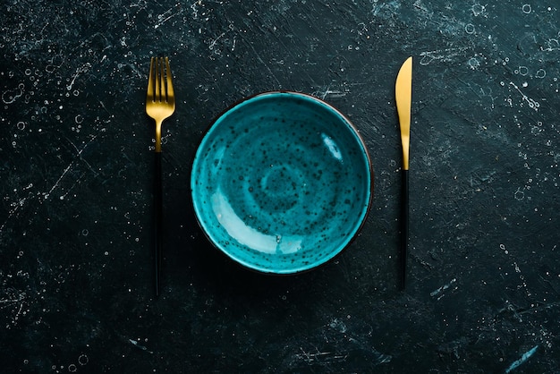 Turquoise plate and cutlery on a black stone background Top view Rustic style