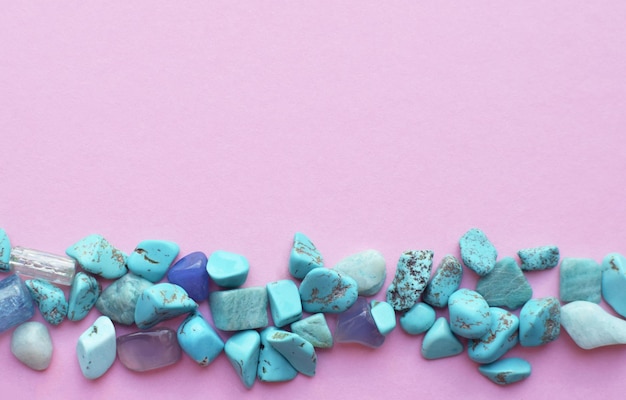 Turquoise semiprecious stones are piled on a pink background Place for text