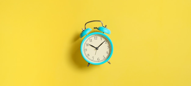 Turquoise vintage alarm clock on yellow background. Top view, flat lay, copy space