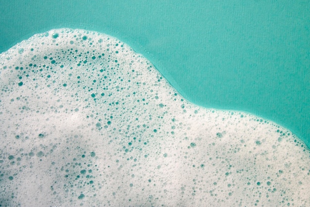 A turquoise water surface with foam in the foreground and a blue background.