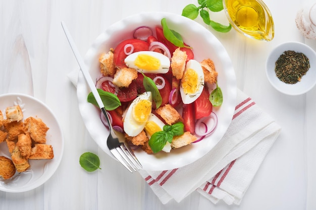 Tuscan Panzanella salad Fresh tomatoes salad with basil leaves eggs olive oil and onion in white bowl on light background Vegetarian panzanella salad Mediterranean healthy food Top view