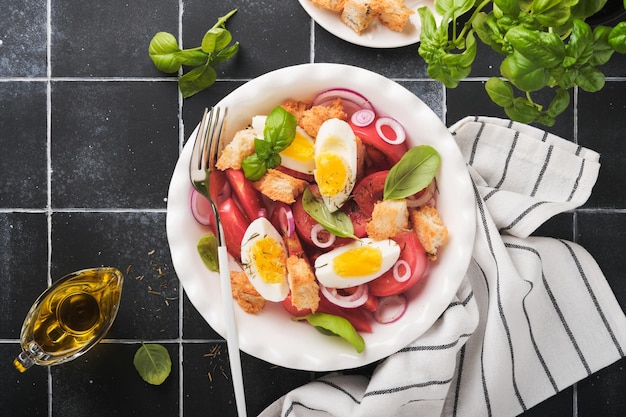 Tuscan Panzanella salad Fresh tomatoes salad with basil leaves eggs olive oil and onion in white bowl on old black background Vegetarian panzanella salad Mediterranean healthy food Top view