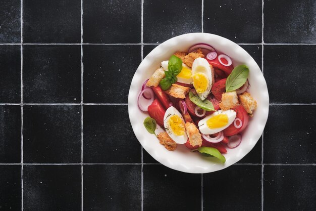 Tuscan Panzanella salad Fresh tomatoes salad with basil leaves eggs olive oil and onion in white bowl on old black background Vegetarian panzanella salad Mediterranean healthy food Top view