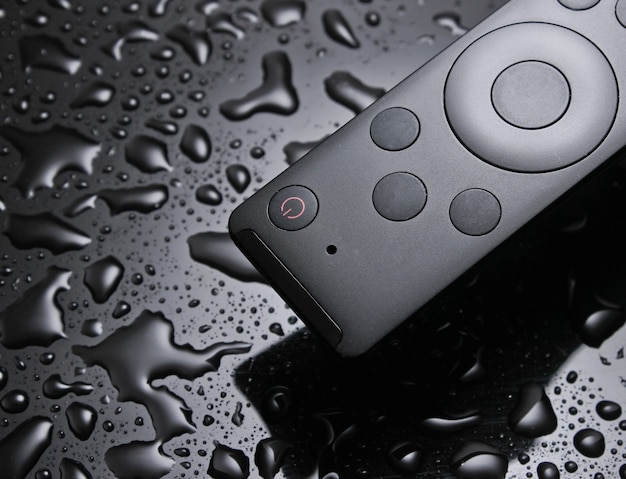 Tv remote closeup on a black background with water drops