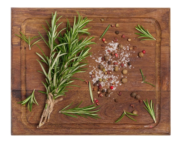 Twigs and leaves of rosemary dry fruits of red black and allspice and salt on a wooden cutting board top view