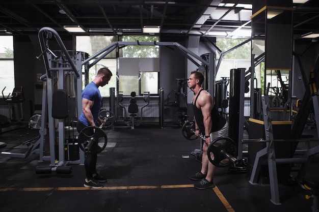 Twin brothers sportsmen facing each other at gym doing barbell deadlift workout