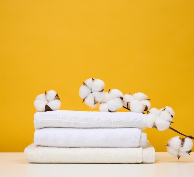 Twisted white terry towels on white table yellow background